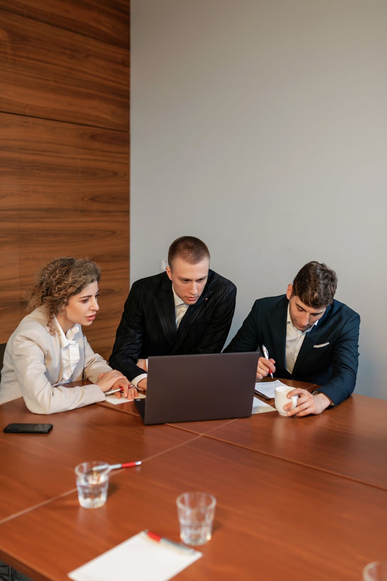 Three colleagues in suits working from a single laptop