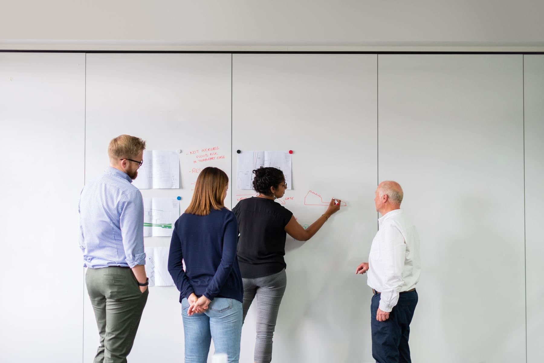 Four colleagues at a wall of printed plans, one writing on it